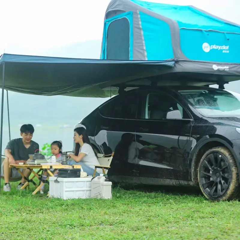 Family camping under Fish Island rooftop tent awning beside black SUV, outdoor picnic and lake scenery