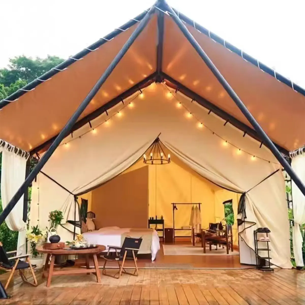 Luxury glamping hotel tent at night with warm string lights, bed and furniture inside, wooden deck and pool in front.