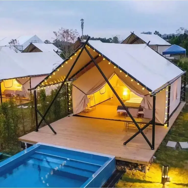 Multiple safari frame tents arranged as a glamping resort at dusk, with wooden decks and pool, warm lighting.
