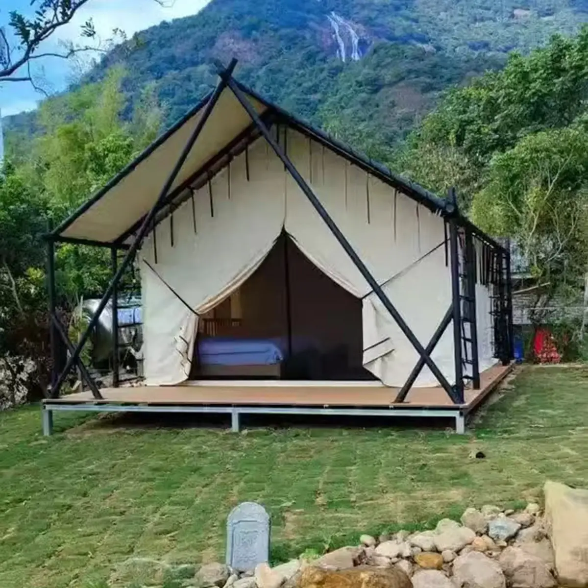 Front entrance of safari frame tent with curtains open, revealing bed inside, wooden deck platform.