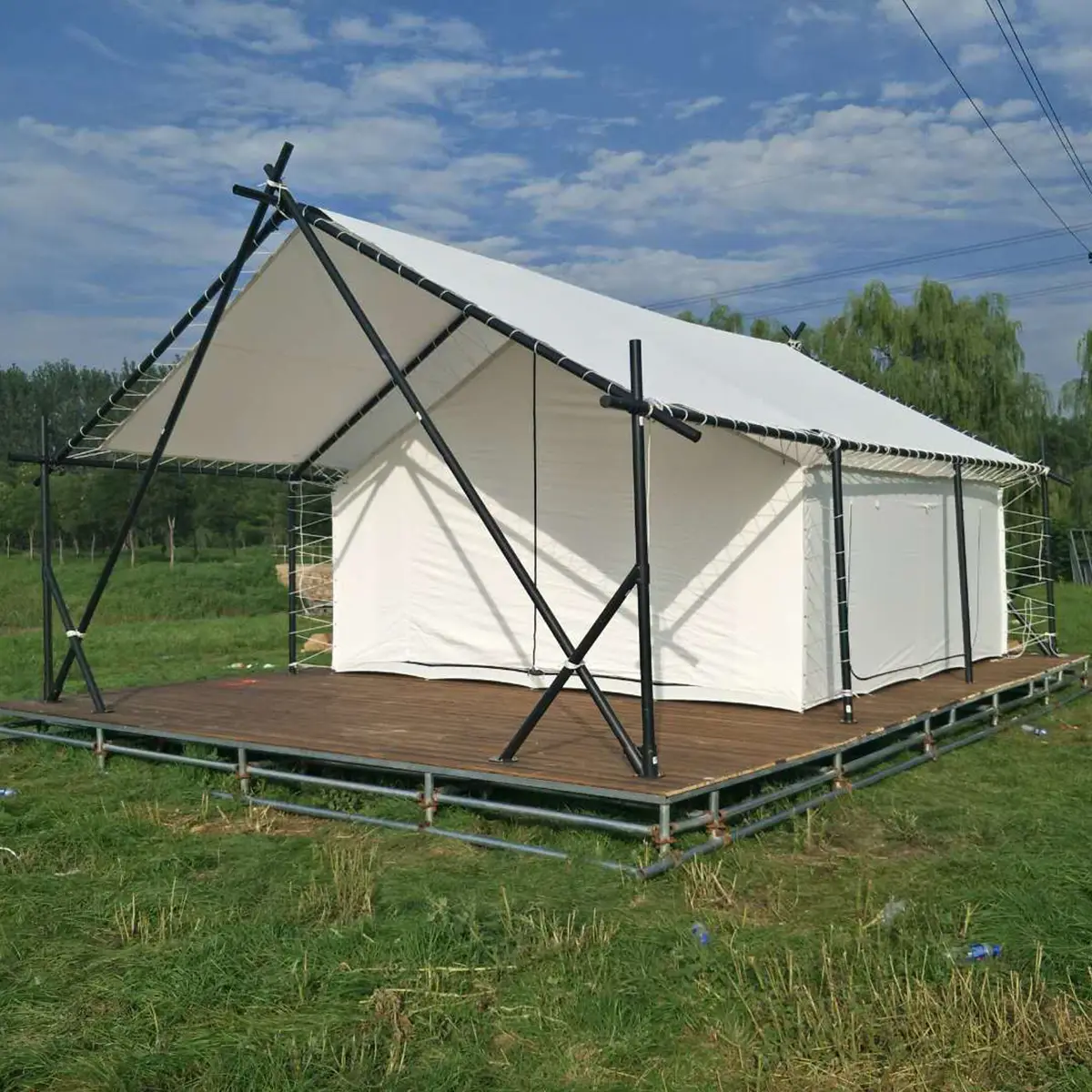 Single luxury glamping hotel tent on grass with wooden deck, white PVC cover and black steel frame, daytime exterior.