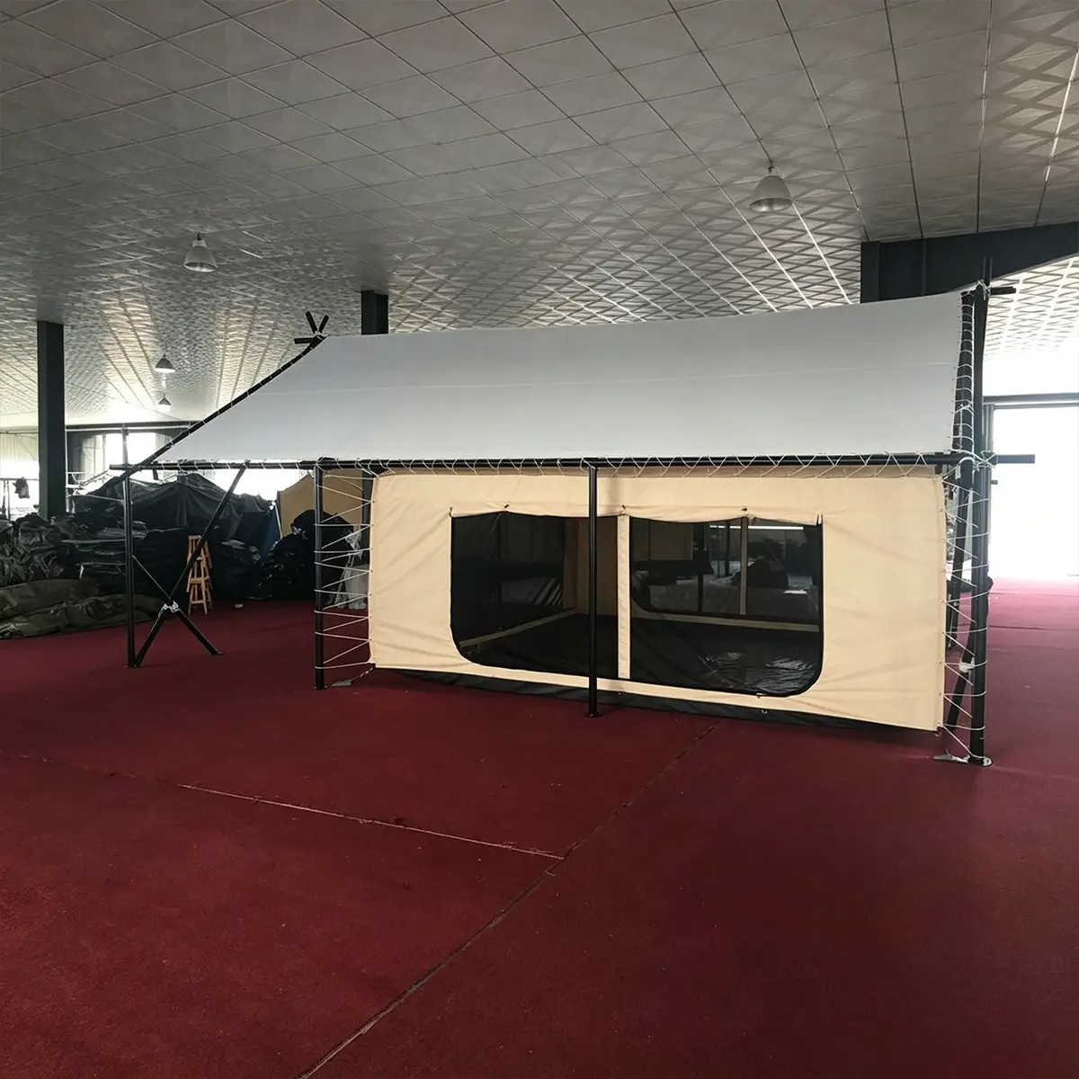Safari frame tent displayed indoors on red carpet, beige outer cover with windows, black steel frame.